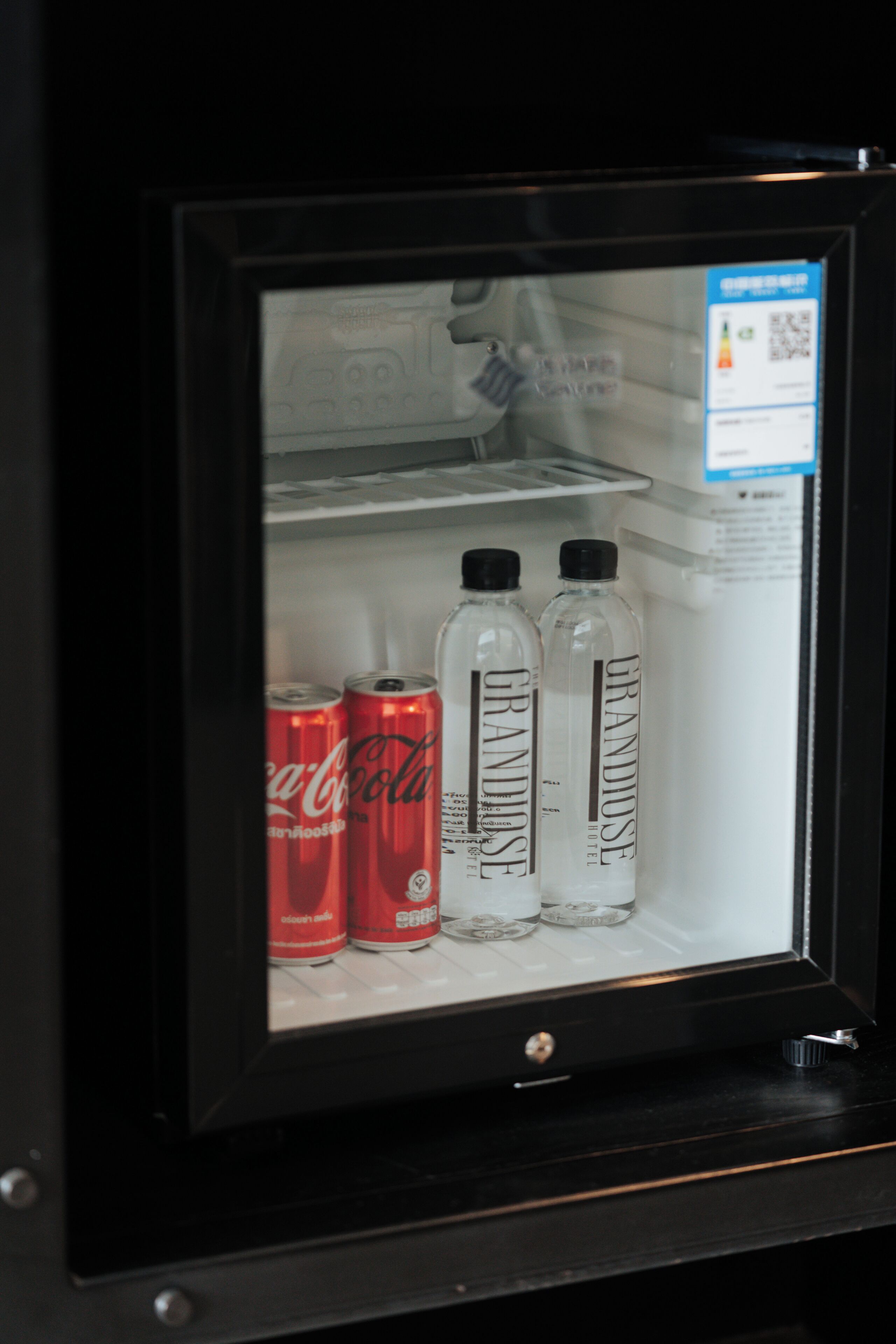 A refrigerator with two Coca-Cola cans and two Grandiose water bottles.