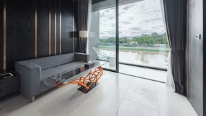 Un salon moderne avec un canapé gris, une table basse en verre et une vue sur un plan d’eau, visible à travers de grandes fenêtres.