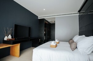 Una habitación de hotel moderna con una cama grande, un televisor de pantalla plana, un banco de madera y un armario de color oscuro.