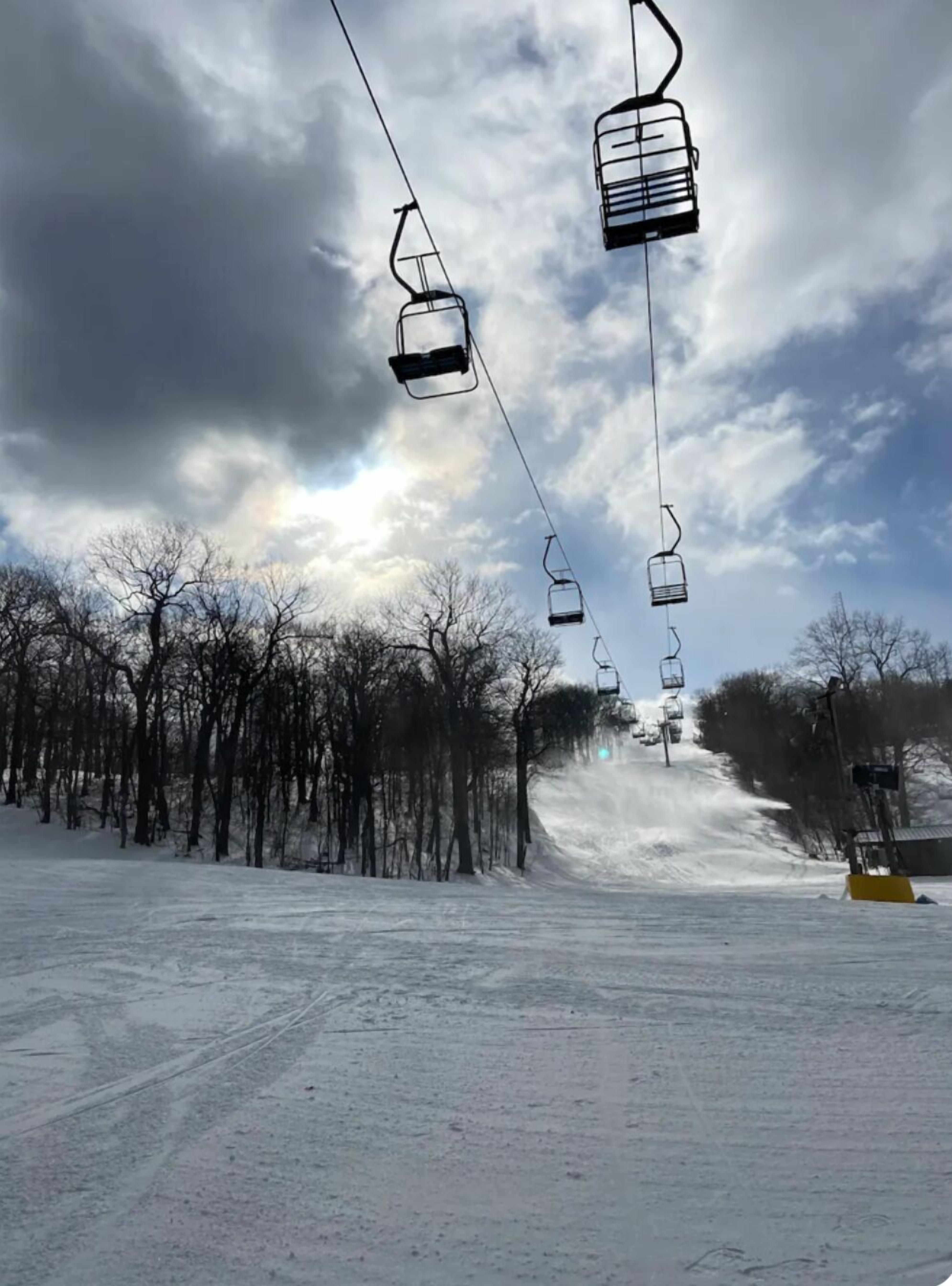 A ski lift with chairs suspended from cables, a snowy landscape, and leafless trees.