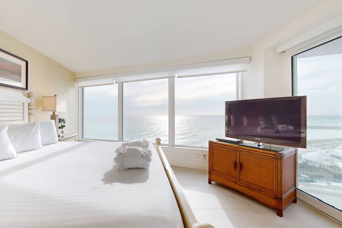 A hotel room with a large bed, a television, and a view of the ocean.