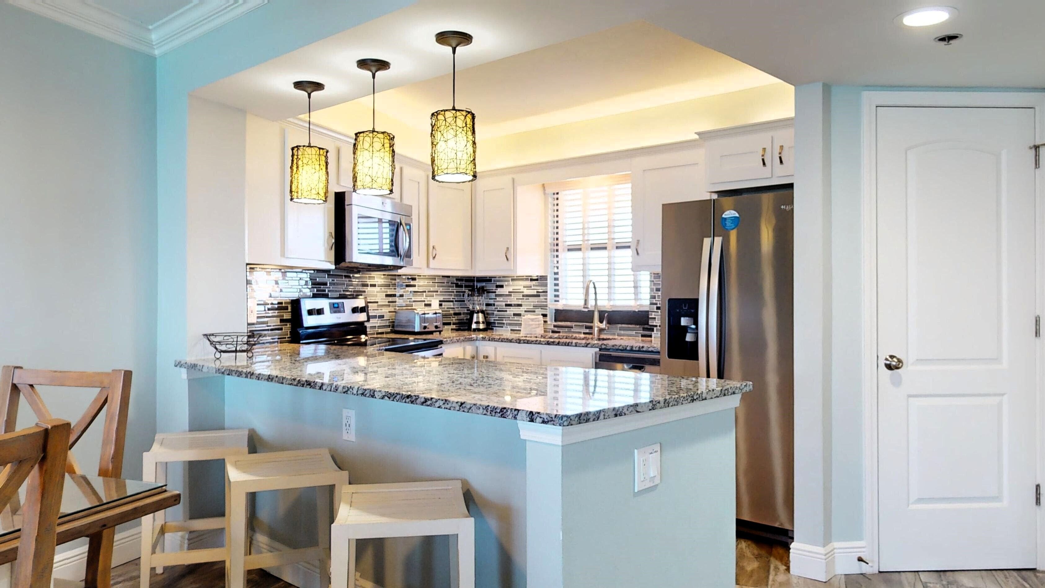 A modern kitchen with granite countertops, stainless steel appliances, and pendant lighting.