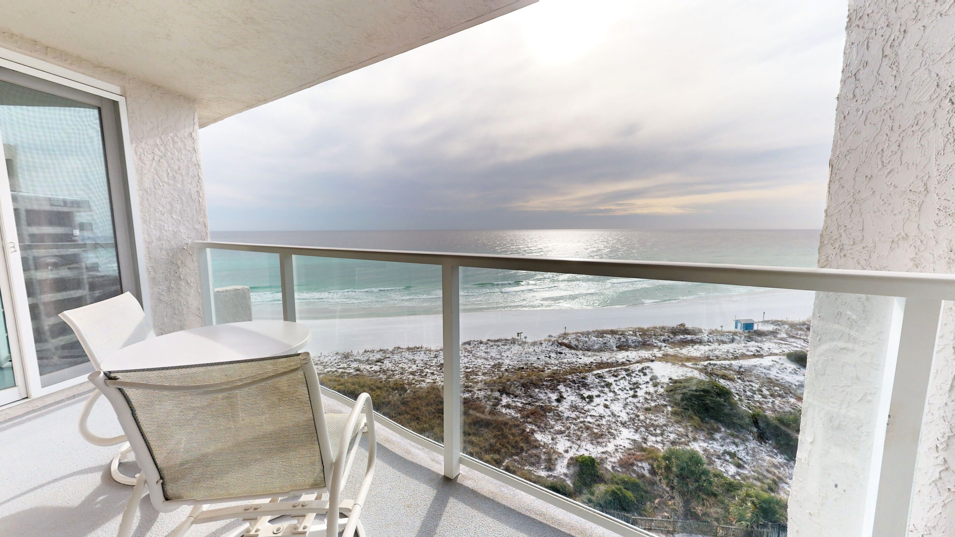 Un balcon avec une chaise et une table blanches, donnant sur une plage dont le paysage est recouvert de neige et offrant une vue sur l’océan.