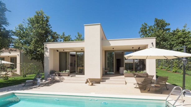 Una casa moderna con piscina, mobiliario de exterior y un jardín bien cuidado.