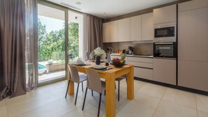 Una cocina moderna con electrodomésticos integrados, un comedor con mesa y sillas, y vista a una piscina a través de amplias ventanas.