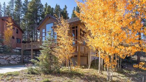 Une cabane en bois dotée d’une terrasse, entourée d’un feuillage automnal et de grands arbres.
