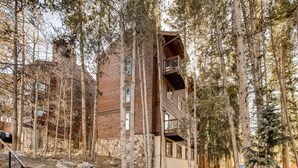 A multi-story wooden cabin surrounded by trees, with a stone base and a balcony on the upper floor. - Spacious, Multi-Level Home Walking Distance to Slopes, Town & Pool (Breckenridge)