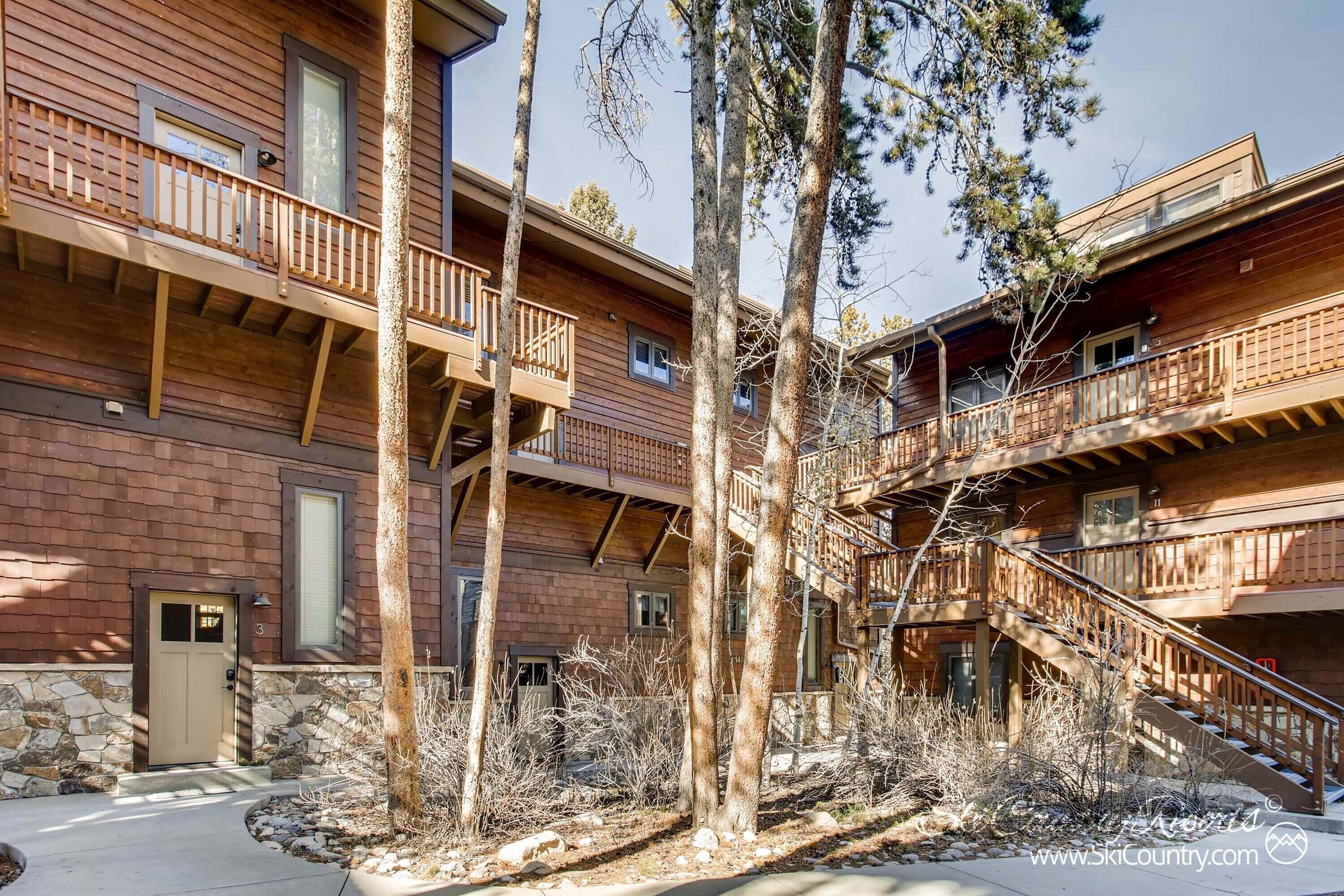 A multi-story wooden building with balconies, a stone entrance, and a clear sky.