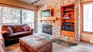A cozy living room with a stone fireplace, a leather sofa, and a television mounted on the wall. - Spacious, Multi-Level Home Walking Distance to Slopes, Town & Pool (Breckenridge)