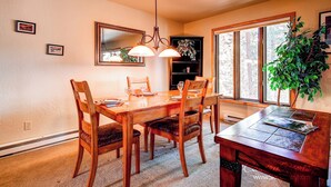 A dining area with a wooden table, chairs, a chandelier, and a large window with a view of trees. - Spacious, Multi-Level Home Walking Distance to Slopes, Town & Pool (Breckenridge)