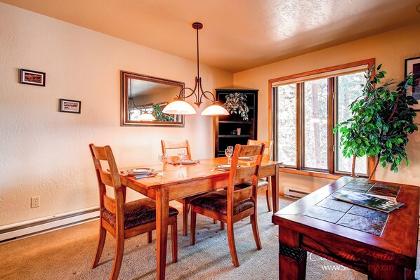A dining area with a wooden table, chairs, a chandelier, and a large window with a view of trees.