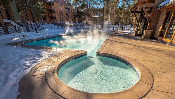 A pool with a steam feature surrounded by a wooden deck, with buildings and trees in the background. - Spacious, Multi-Level Home Walking Distance to Slopes, Town & Pool (Breckenridge)