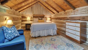 Een slaapkamer in een blokhut met een bed, een dressoir en een blauwe bank.