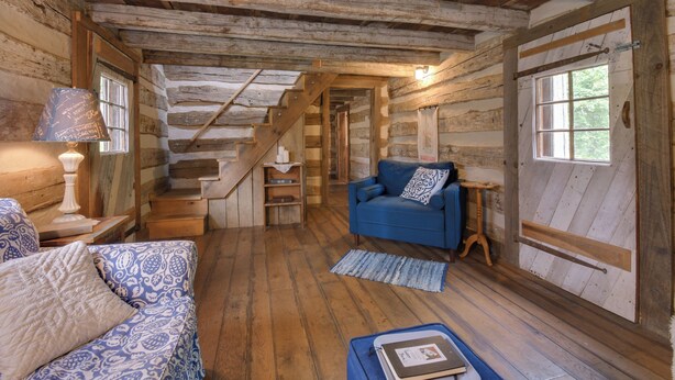 Een rustiek houten interieur met een wenteltrap, een blauwe bank en een kleine tafel met boeken.