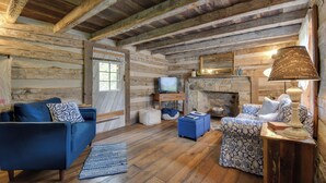Een rustiek houten interieur met een houten plafond, een stenen openhaard, een televisie en een bank met decoratieve kussens.