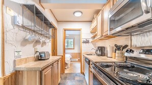 A narrow kitchen with wooden cabinets, a stove, and a microwave. There is a window in the background. - RECENTLY REMODELED! Beautiful Condo w/ Fantastic Central Location | PM1B (Breckenridge)