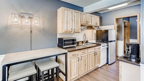A compact kitchen with wooden cabinets, a microwave, a stove, and a coffee maker.