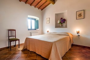 A bedroom with a bed, a chair, a window, and wall-mounted lights.