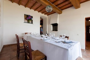 A dining area with a long table set for a meal, wooden chairs, a hanging light fixture, and a small window with flowers.