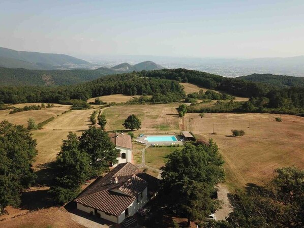 A rural property with a swimming pool, surrounded by fields and trees, with a view of distant hills.