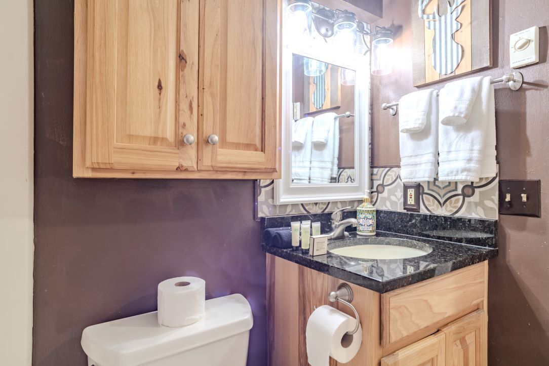 A bathroom with wooden cabinets, a sink with a marble countertop, and a mirror above the sink.