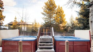A hot tub area with two hot tubs, wooden steps leading up to them, and a wooden fence in the background.