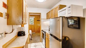 A compact kitchen with wooden cabinets, a stainless steel refrigerator, a microwave, and a toaster.