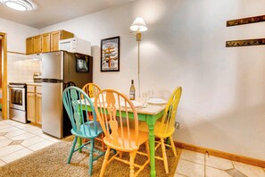 A compact kitchen with wooden cabinets, a refrigerator, a microwave, and a dining table with colorful chairs. - Economical, Cozy Condo Near Main St Access to Spacious Lobby, Hot Tubs | PM5B (Breckenridge)