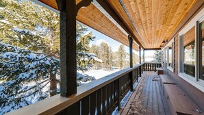 A wooden deck with a railing overlooking a snowy landscape with trees.