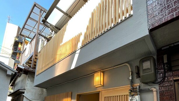 A modern two-story building with a balcony, a door with a wooden slat design, and a small outdoor area with a drain. - Tamatsukan (Osaka)