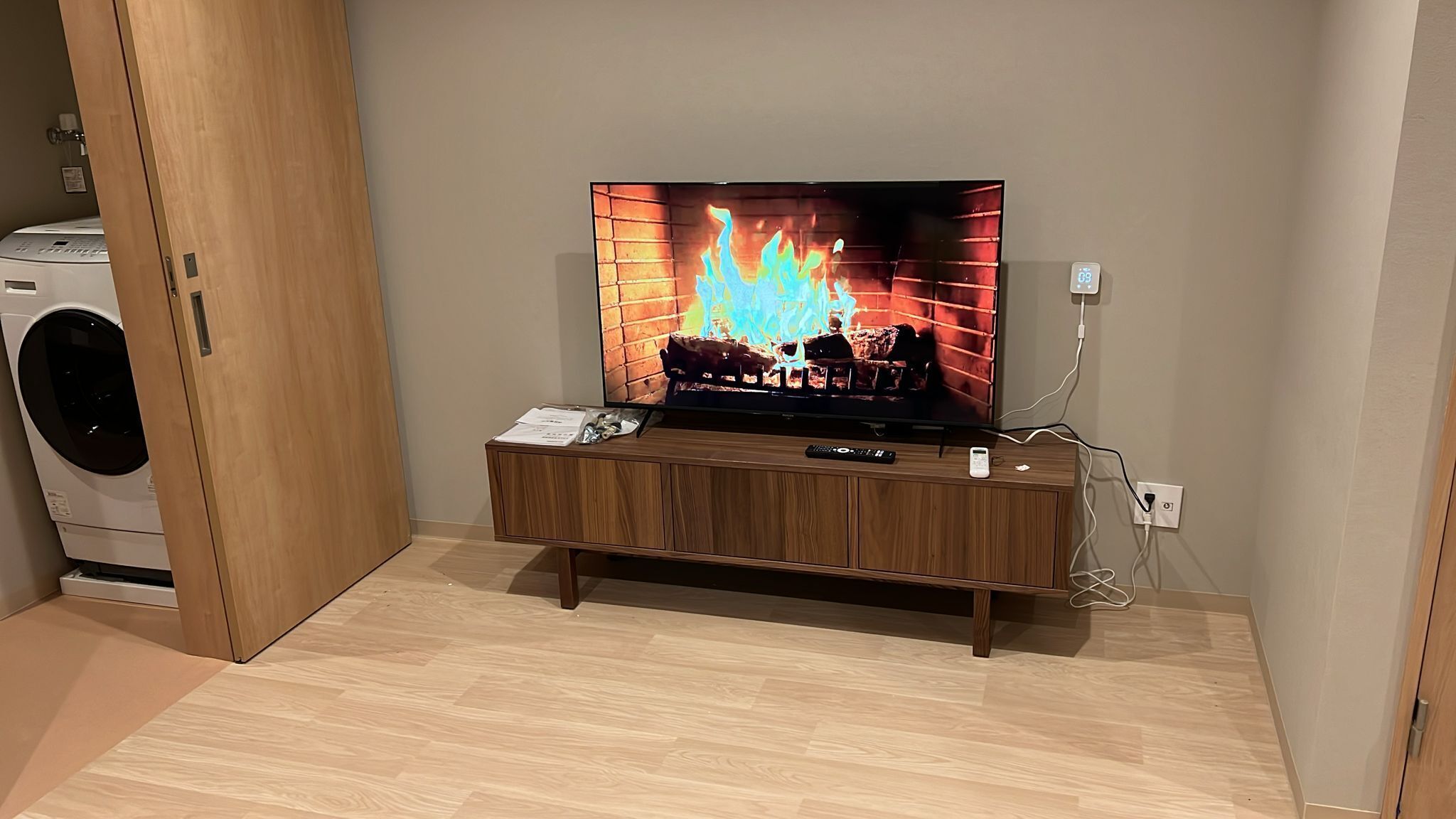 A living room with a television displaying a fireplace, a washing machine, and a wooden cabinet.