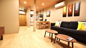 A modern living room with a sofa, two wooden side tables, and a dining area with chairs. - Tamatsukan (Osaka)