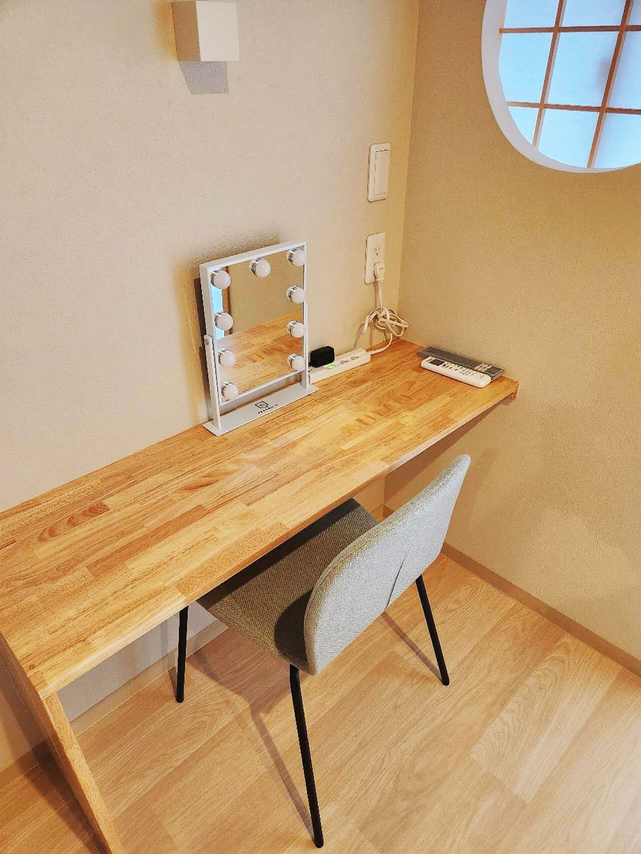 A wooden desk with a vanity mirror and lights, a chair, and a window with a view.