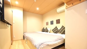 A bedroom with a bed, a flat-screen TV mounted on the wall, and an air conditioning unit. - Tamatsukan (Osaka)