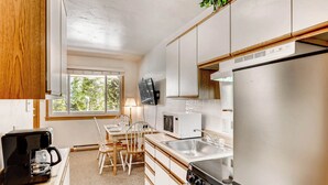 Une cuisine de taille réduite équipée d’un four à micro-ondes, d’une cuisinière, d’un évier et d’armoires en bois.