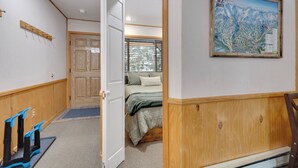 A hotel room with a wooden floor, a bed with a green blanket, a wooden door, a map on the wall, and a coat rack. - Centrally Located Gem. Affordable & Efficient. Onsite Hot Tubs | PM7A (Breckenridge)
