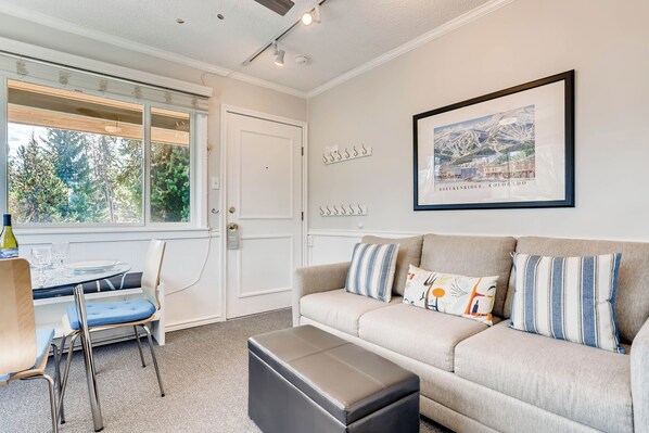 A living room with a beige sofa, striped pillows, a glass coffee table, and a blue cushioned chair.