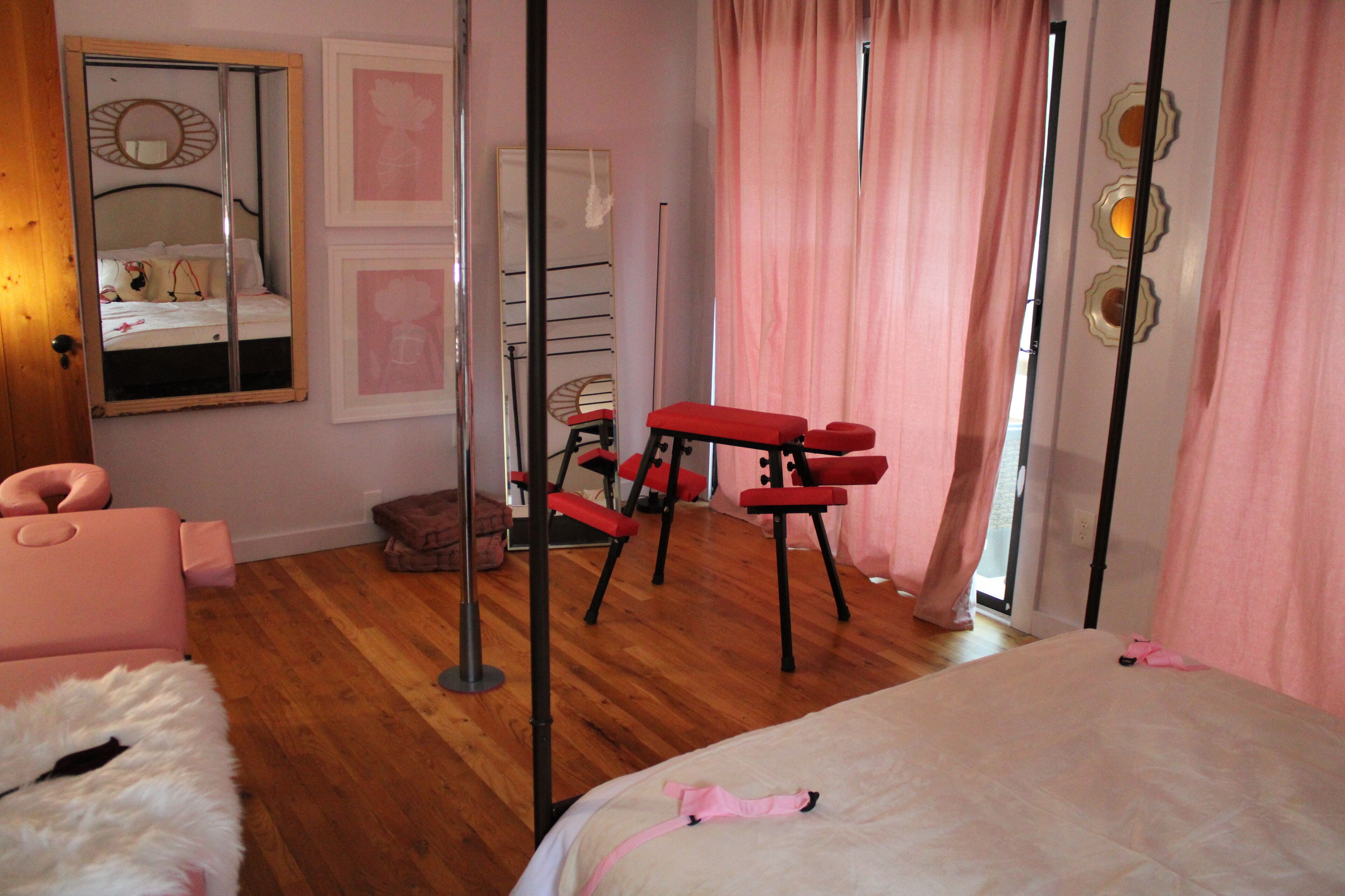 Ein Schlafzimmer mit einem Bett, einem Spiegel, einer roten Bank und rosafarbenen Vorhängen.