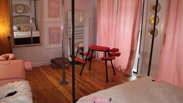 Ein Schlafzimmer mit einem Bett, einem Spiegel, einer roten Bank und rosafarbenen Vorhängen.
