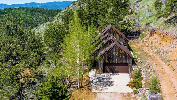 A cabin with a sloped roof, surrounded by dense forest and mountains in the background.