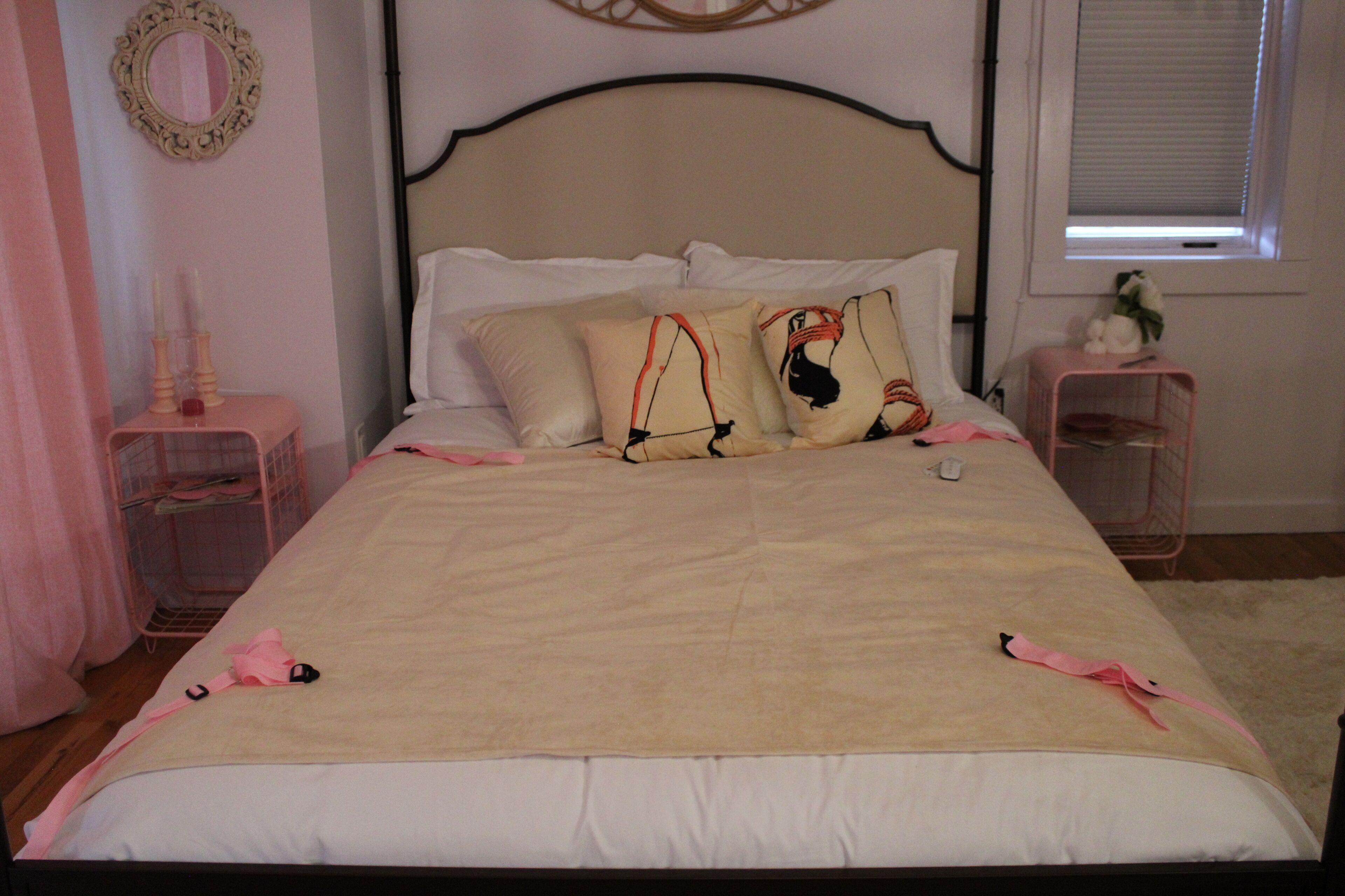A neatly made bed with a white and beige color scheme, two bedside tables with pink accents, and a mirror on the wall.