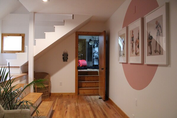 Una escalera que lleva a un segundo piso, suelo de madera, una silla de mimbre y cuadros en la pared.