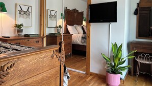 A bedroom with a wooden bed, a large mirror, a television, and two potted plants.