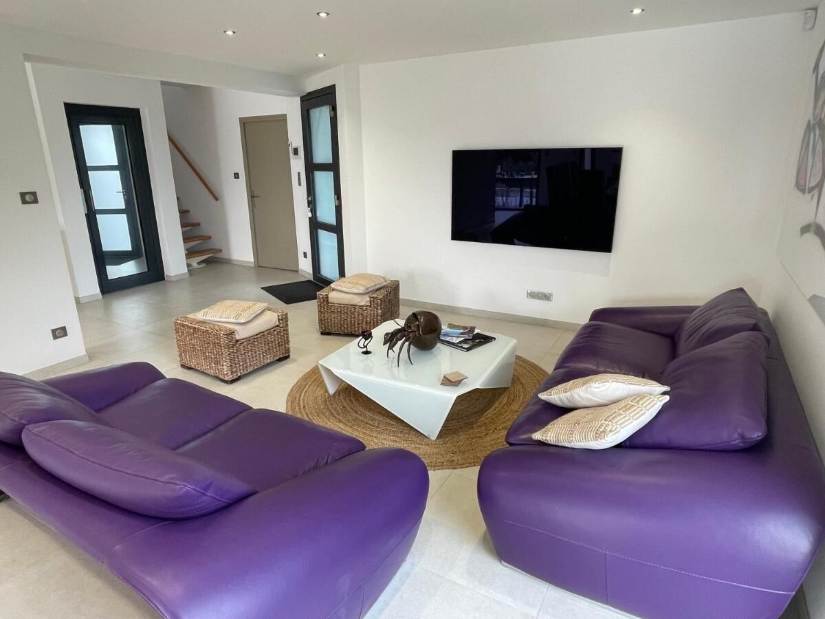 A modern living room with a large flat-screen TV mounted on the wall, a sofa set, a coffee table, and wicker side tables.