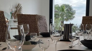 A dining table set with wine glasses, a bowl, and cutlery, with a view of palm trees and a building through a window. - METERS FROM THE MEDITERRANEAN AMID ST. TROPEZ & ST. MAXIM (Roquebrune-sur-Argens)