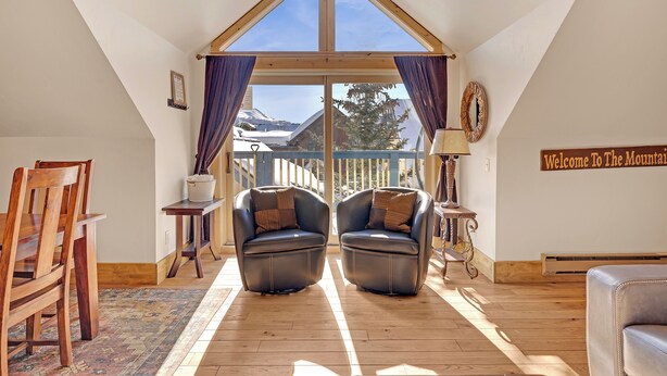 A cozy room with a wooden floor, two leather armchairs, a wooden dining table, and a view of a mountain through a large window. - Unbelievable Downtown, Walk Everywhere. Pet Friendly! Private Hot Tub! SCC4 (Breckenridge)