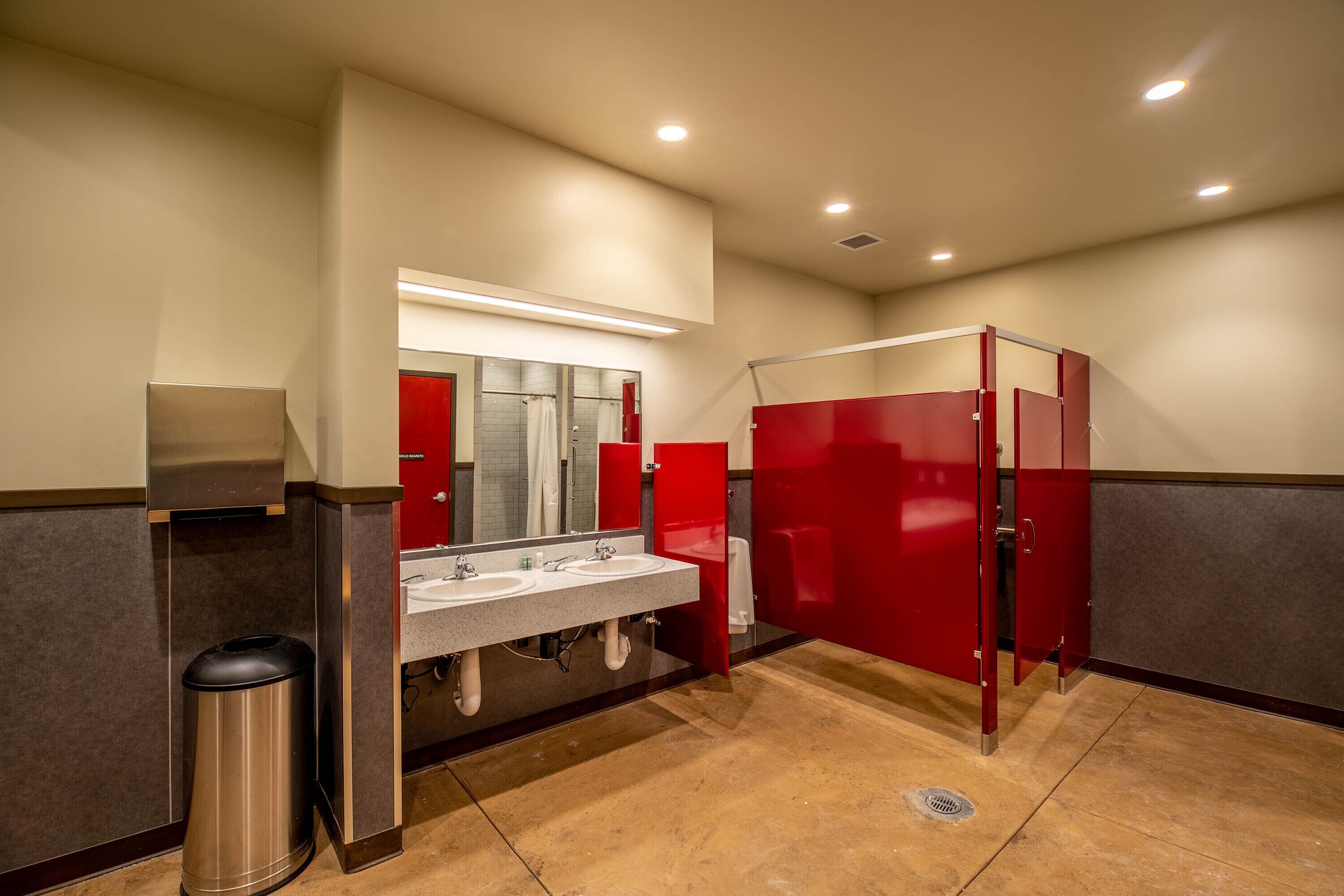 Un bagno pubblico con due lavandini, un cestino e cabine rosse.