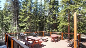 A wooden deck with picnic tables and a grill, surrounded by tall pine trees. - Budget Friendly Hotel Lock Off Steps from the Slopes (Breckenridge)