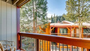 Un balcon en bois, agrémenté de chaises en osier, qui offre une vue sur un immeuble doté d’un toit rouge et de nombreuses fenêtres.