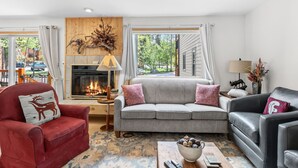 Ein gemütliches Wohnzimmer mit Kamin, einem roten Sessel, einem grauen Sofa und einem schwarzen Ledersessel.